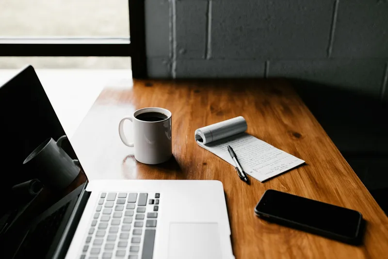 Postazione di lavoro con taccuino, laptop e caffè — l'ambiente tipico di chi lavora nella comunicazione